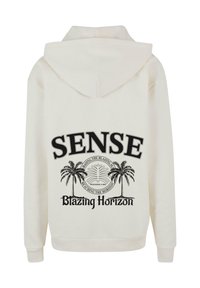 Lys kremfarget hettegenser med et stort svart trykk på baksiden med ordene "SENSE" og "Blazing Horizon" pyntet med palme grafikk.