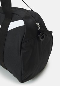 Black duffel bag made of durable material, featuring a white stripe, zip closure, sturdy handles, and a side pocket with pull tab.