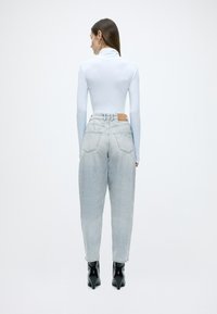 Valge pika varrukaga topp kombineeritud hele siniste lahtiste teksadega, millel on nahast patch tagaküljel. Mustad kontsaga saapad täiendavad komplekti.