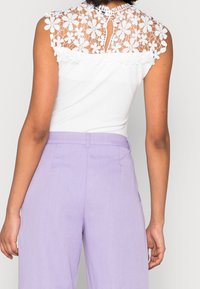 Vit topp med blommig spetsbak och korta ärmar, tillsammans med ljuslavendel höga byxor med en slät textur och klassisk passform.