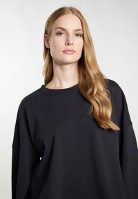 Schwarzer oversized Pullover mit Rundhalsausschnitt und überschnittenen Schultern. Glatte Baumwolltextur, minimalistisches Design, ohne sichtbare Muster oder Beschläge.