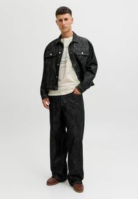 Donkerdenim jasje met bijpassende wijde broek, aangevuld met een lichtcrème t-shirt met tekst. Casual stijl met contrasterende stiksels.