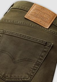 Zielone oliwkowe dżinsy Levi's z tylną kieszenią, na której widnieje brązowa skórzana metka Levi Strauss & Co. z rozmiarem W32 L32.