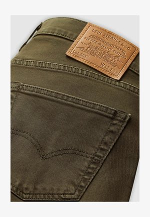 Olijfgroene Levi's jeans achterzak met een bruin leren label van Levi Strauss & Co. waarop de maat W32 L32 staat.