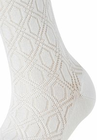 Weiße Baumwollsocke mit einem strukturierten Rautenmuster in einem helleren Beige. Ihre Form ist typisch für knöchellange Socken mit einer glatten Oberfläche.