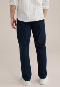 Mornarsko modri hlače iz bombaža, s straight-leg obliko. Model nosi bele superge. Gladka tekstura, minimalno podrobnosti.