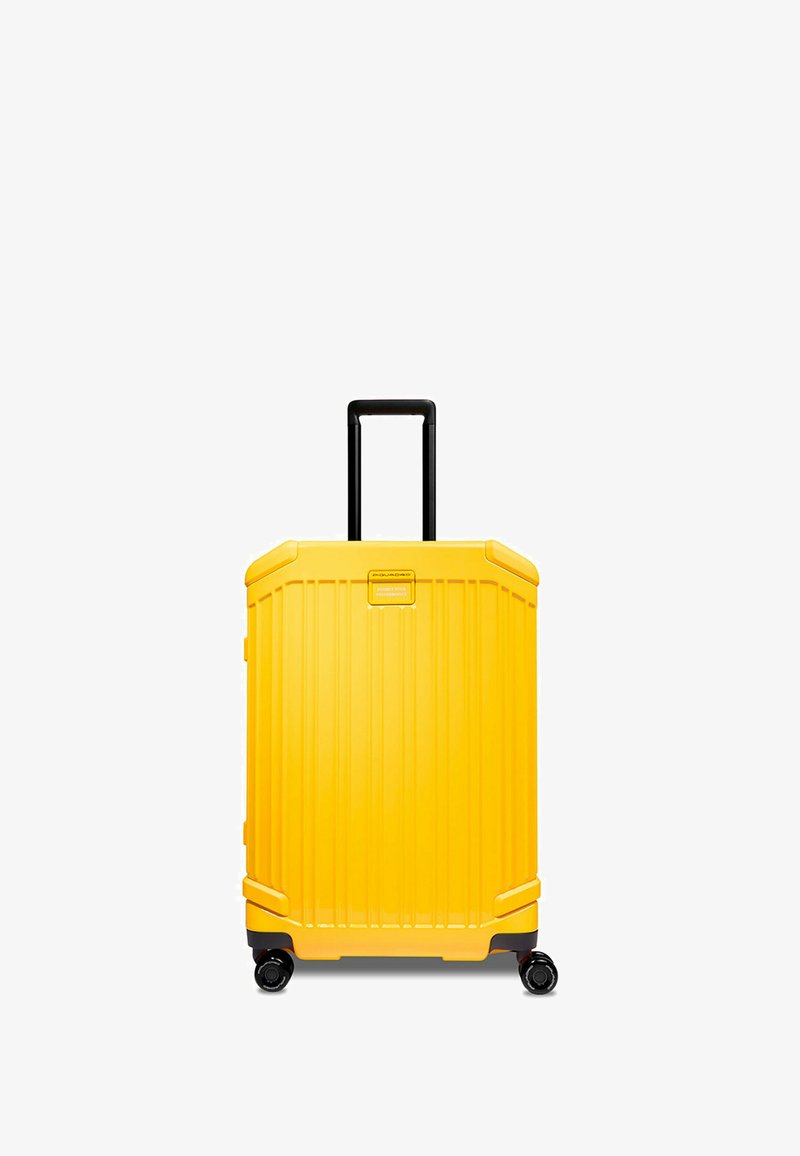 Valigia a cabina gialla con guscio rigido, texture a righe verticali, manico nero retrattile e quattro ruote nere per una facile mobilità.