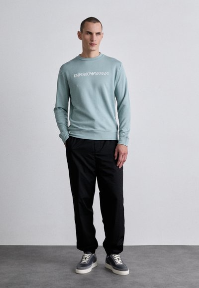 Helesinine vaade sweatshirt valge "Emporio Armani" logoga, koos mustade pükstega ja hallide spordijalatsitega, millel on kreemjas tallad. Sile tekstuur.