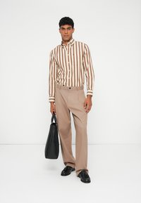 Ριγέ καφέ και κρέμα πουκάμισο με κουμπιά σε συνδυασμό με μπεζ παντελόνι. Μαύρη τσάντα στο χέρι, μαύρα παπούτσια. Απλός σχεδιασμός, δομημένη εφαρμογή.