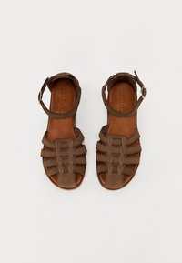 Sandales en daim marron avec une bride à la cheville et un design entrecroisé, dotées d'une semelle en cuir lisse marron et d'un bout ouvert.
