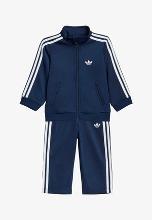 Marineblauw peutertrainingspak met witte Adidas-strepen op mouwen en broekspijpen, jas met ritssluiting en elastische manchetten.