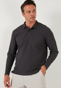 Camisa polo de manga larga en gris oscuro, hecha de un tejido texturizado con cuello, botonera de dos botones y un corte relajado.