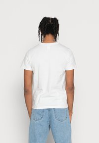 Camiseta de algodón blanca lisa, de manga corta, con cuello redondo, vista trasera. Combinada con jeans de mezclilla azul claro. Sin patrones ni logotipos visibles.