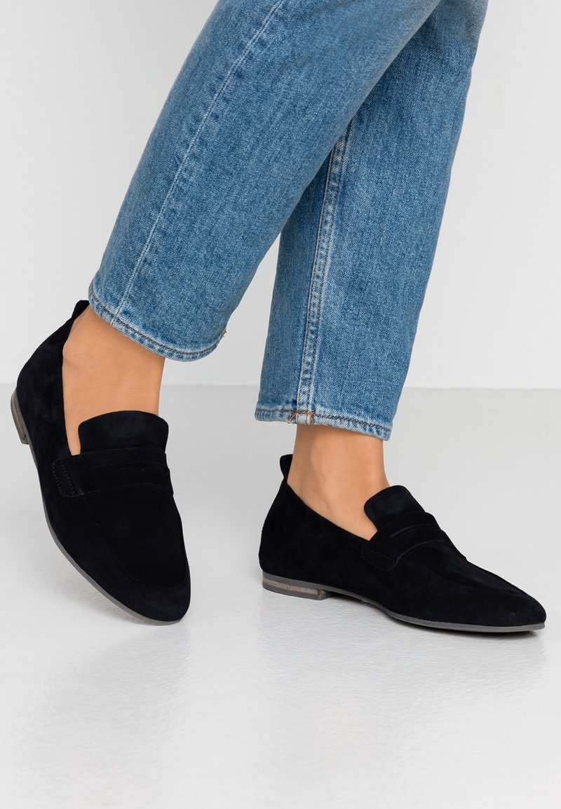 Chaussures en suede noir à talon plat, avec un bout arrondi et un détail de bride superposée, assorties à un jean court bleu clair.