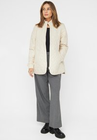 Light beige quilted jacket with a high collar and side pockets, paired with grey wide-leg trousers and black lace-up boots.
