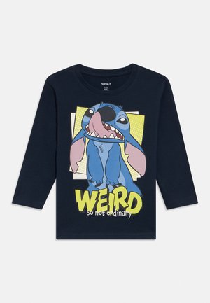 Chemise à manches longues bleu marine avec un personnage de dessin animé. Présente un personnage bleu et rose avec le mot "WEIRD" en texte gras jaune et blanc.