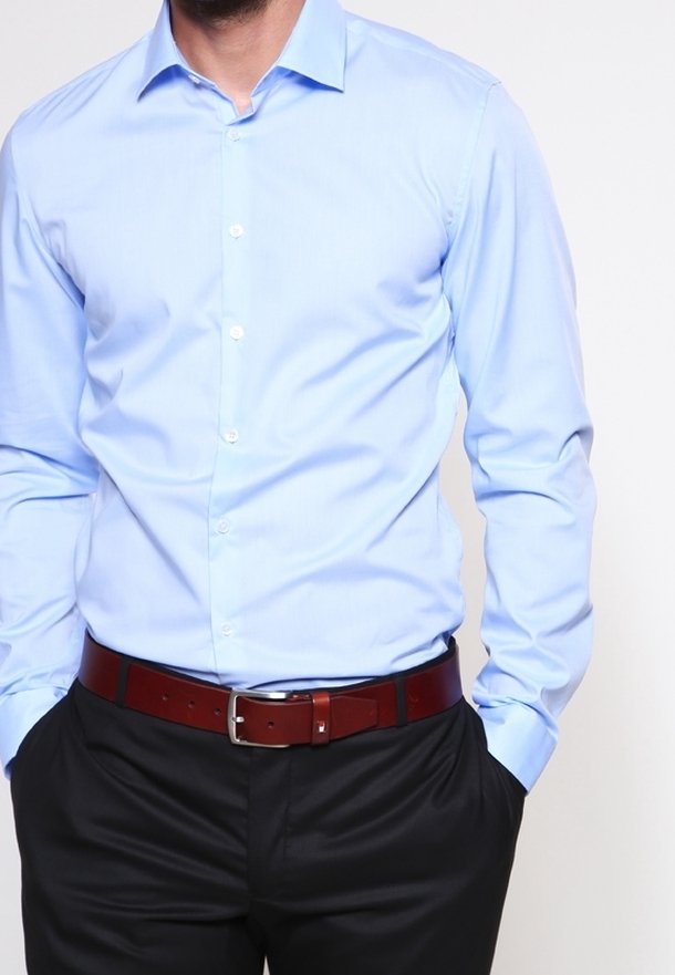 Ljusblå långärmad skjorta med knappstängning, spetsig krage och slät yta, tillsammans med ett mörkt bälte och svarta byxor.