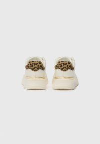 Sko med en kremfarget overdel, leopardskinn detalj på hælen, og gullfarget stripe. Har en teksturert såle og avrundet form.