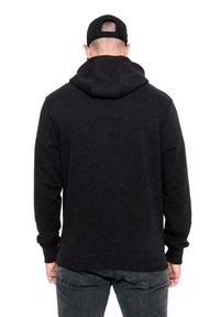Felpa nera con cappuccio regolabile, morbido al tatto e con polsini a coste. Indossata con jeans grigio scuro, presenta un design semplice e pulito.