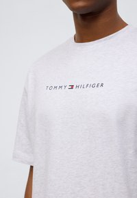 Ανοιχτό γκρι βαμβακερό t-shirt που διαθέτει εμφανές λογότυπο «TOMMY HILFIGER» σε ναυτικό μπλε, κόκκινο και λευκό στο μπροστινό μέρος. Κοντά μανίκια, στρογγυλή λαιμόκοψη.