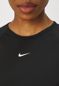 Camiseta deportiva negra con cuello redondo. Presenta un pequeño logo blanco de Nike en el centro. Textura suave, con mangas raglán cortas.