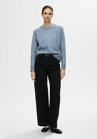 Lichtblauwe gebreide trui, ronde halslijn, gecombineerd met hoge zwarte wijde broek en zwarte platte schoenen. Eenvoudig ontwerp, minimale details.