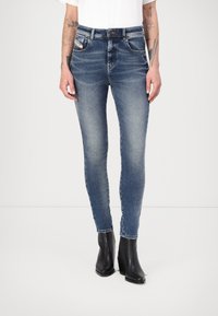 Uske skinny traperice u tamnoplavoj boji, s umjerenim strukom, dizajnom od pet džepova i suptilnim izbjeljivanjem. Uparene s crnim čizmama na petu.