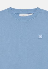 Felpa leggera azzurro chiaro a girocollo in cotone, con colletto e polsini a costine, dotata di una piccola etichetta con il logo bianco di Calvin Klein sul petto.
