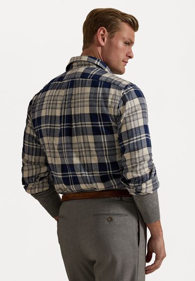 Gecarieerd shirt in marineblauw, crème en grijs, met lange mouwen opgerold. Vergezeld van grijze broek, met achterzak en knoopdetails.
