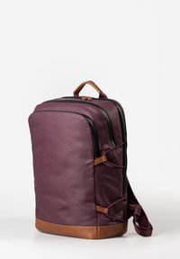 Zaino in ecopelle viola con dettagli in pelle marrone, due scomparti con zip, una maniglia superiore e cinghie elastiche laterali per ulteriore spazio di stoccaggio.