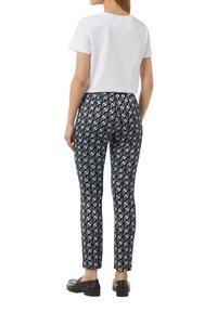 Zwart-wit gestreepte broek met een geometrisch ontwerp, gecombineerd met een effen witte shirt met korte mouwen. Model draagt zwarte instappers.