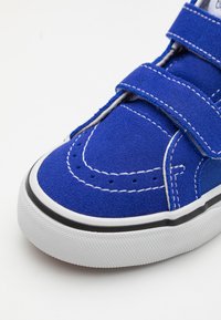 Zapatillas de ante azul con un upper texturizado, costuras blancas, correas de gancho y bucle, y una suela de goma negra con agarre texturizado.
