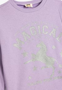 Fioletowy sweatshirt z ribbowanym kołnierzem, ozdobiony srebrnym brokatowym napisem oraz grafiką jednorożca otoczoną gwiazdami. Miękka struktura, swobodny styl.