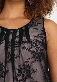 Černý krajkový top s propracovanými květinovými vzory, průhlednou strukturou a výstřihem do lodi s jemně skloubenými detaily.