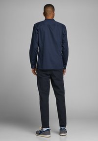 Camicia a maniche lunghe blu navy con orlo dritto, abbinata a pantaloni scuri strutturati. L'outfit presenta scarpe casual con accenti blu e grigi.