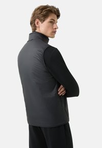Czarna bezrękawnikowa kamizelka z wysokim kołnierzem, wykonana z gładkiego, pikowanego materiału. Posiada dopasowany krój z dyskretnymi detalami szwów.