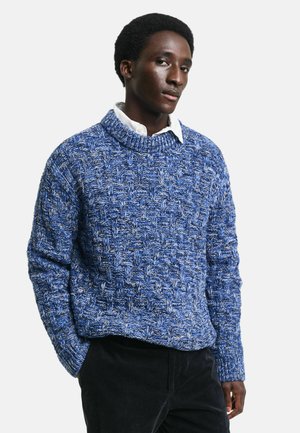 Blue knitted sweater with a textured pattern, featuring a crew neck and long sleeves. Worn over a white collared shirt.