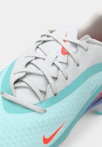 Παπούτσι ποδοσφαίρου Nike με ανοιχτό μπλε και λευκό επάνω μέρος, γκρι κορδόνια και πορτοκαλί λογότυπο. Υφή σόλας με μωβ και ροζ λεπτομέρειες.