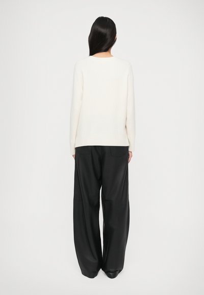 Cream sweater with a round neckline and long sleeves, paired with black wide-leg trousers, featuring a smooth texture and two back pockets.
