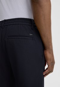 Pantaloni navy con elastico in vita e finitura testurizzata, dotati di una tasca posteriore e un piccolo etichetta della marca cucita.