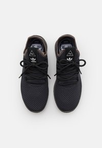 Svarta träningsskor med överdel i mesh, rund tå, kontrasterande bruna accenter och platta snörningar. Har märkta etiketter på tungan.