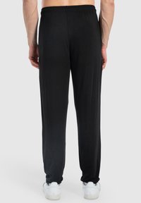 Schwarze, leichte Hose mit elastischem Bund, geraden Beinen und weicher Textur. Getragen mit weißen Sneakers, ohne sichtbare Muster oder Akzente.