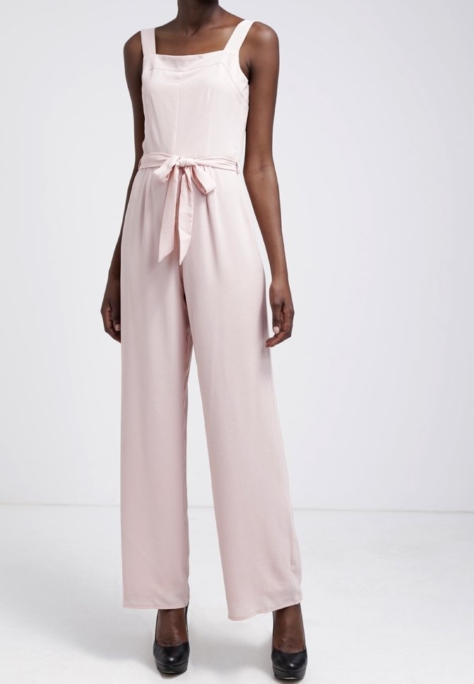 Vaaleanpunainen haalarimaha, jossa on neliökaula-aukko, leveät hihnat ja solmittava vyötärö. Kankaan pinta on sileä; löysät housut ulottuvat lattiaan. Mustat korot on käytössä.