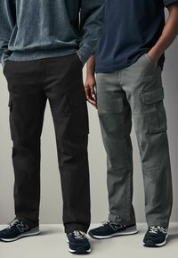 Schwarz-weiß Cargo-Hose mit mehreren Taschen, aus strapazierfähigem Stoff gefertigt. Die Hose hat ein gerades Bein-Design und eine leicht strukturierte Oberfläche.