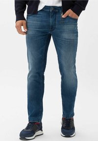 Jeans de denim en un lavado medio con un ajuste slim. Presenta una cremallera y cierre de botón, y un ligero efecto de desgaste. Combinados con zapatillas deportivas.