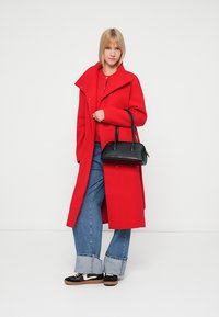 Rød ullblanding lang kåpe, svart håndveske, rød topp, vide denimbukser med oppbrett, svart og hvite sneakers. Enkel, ren design.