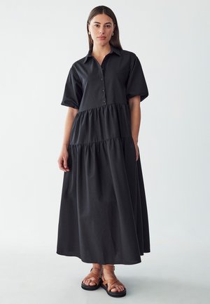 Abito nero a maniche corte, con bottoni e design a strati. Realizzato in tessuto morbido, presenta una vestibilità comoda e un orlo lungo fino alla caviglia.