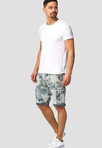 T-shirt blanc à manches courtes associé à un short cargo à motifs avec des designs floraux verts et bleus. Porté avec des baskets blanches.