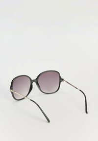 Czarne okulary przeciwsłoneczne w oversize z gradientowymi szarymi soczewkami. Gładka plastikowa oprawa z złotymi metalowymi akcentami na świątkach. Zakrzywiony, elegancki design.