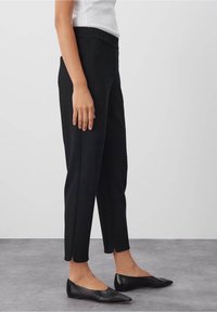 Svarta strukturerade byxor med smal passform och elastisk midja, i kombination med svarta ballerinas. Tyget är mjukt och något elastiskt.